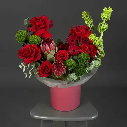 Цветочная композиция из красных роз, молюцеллы и протеи в шляпной коробке